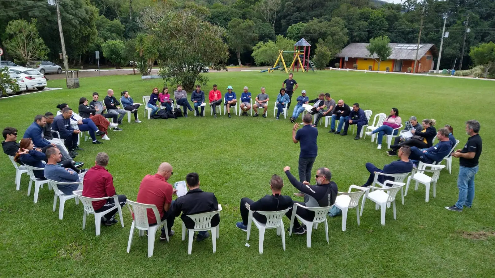 roda de grande número de pessoas sentadas em cadeiras num vasto gramado com duas pessoas da Quadrat palestrando